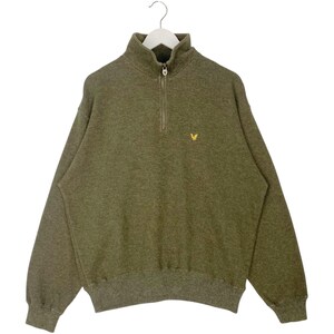 Puede incluir: Sudadera verde oliva con cierre de cremallera de cuarto de cuello y un peque&ntilde;o logotipo de p&aacute;jaro amarillo en el pecho. La sudadera tiene cuello alto y pu&ntilde;os y dobladillo acanalados. Colgada en una percha blanca.