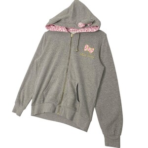 May include: A gray zip-up hoodie with a hood featuring pink leopard print lining and small ear-shaped details. The front has a pink bow design with gold embroidery and the words "Hello Kitty".