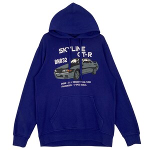 May include: A blue hooded sweatshirt featuring a graphic of a gray sports car with the text "SKYLINE CT-R BNR32". Below the car are the words "ENGINE: 2.6 L RB26DETT TWIN-TURBO TRANSMISSION: 5-SPEED MANUAL". The sweatshirt has a kangaroo pocket.