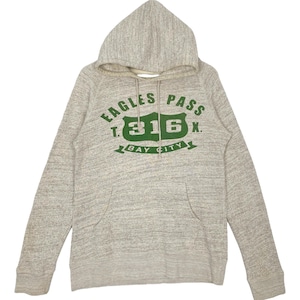 Puede incluir: Una sudadera con capucha de color gris claro con cordón y bolsillo delantero. La parte delantera de la sudadera presenta un gráfico verde que dice "EAGLES PASS T. 316 X. BAY CITY". La sudadera está hecha de un material suave y texturizado.