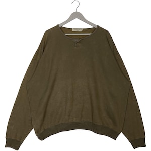 Può includere: Una felpa verde oliva a maniche lunghe con scollo tondo e paramontura a tre bottoni. La felpa è appesa a un'appendiabiti grigio. Il nome del marchio è visibile sul collo.