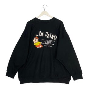 May include: Black sweatshirt with the text "I'M JAIKO" and a cartoon character illustration. The character is wearing a yellow shirt, red shorts, and a hat. Additional text below the character describes the character.