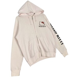 May include: A light pink zip-up hoodie featuring the Hello Kitty character on the front and the words "HELLO KITTY" printed below. The right sleeve has the words "HELLO KITTY" printed vertically in black. The hoodie has a hood and two front pockets.
