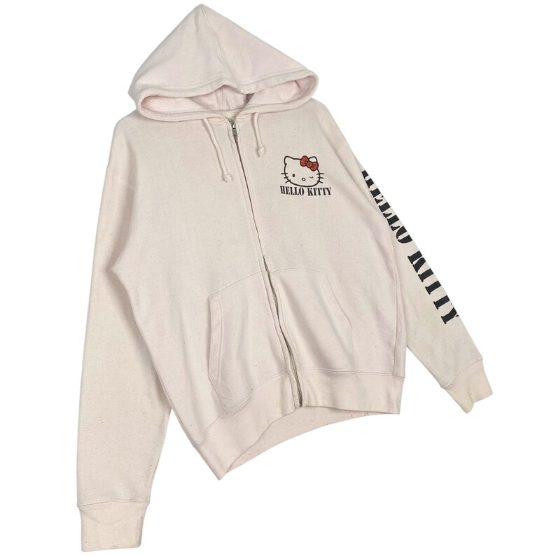 May include: A light pink zip-up hoodie featuring the Hello Kitty character on the front and the words "HELLO KITTY" printed below. The right sleeve has the words "HELLO KITTY" printed vertically in black. The hoodie has a hood and two front pockets.