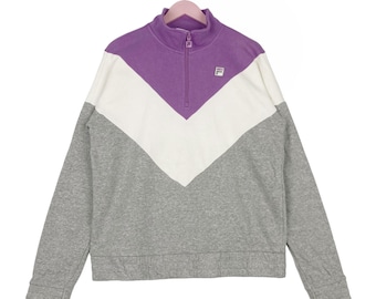May include: A gray, white, and purple quarter-zip sweatshirt with a small logo on the chest. The sweatshirt has a color-blocked design with a V-shaped pattern.
