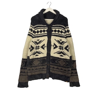 May include: A patterned cardigan with a shawl collar, in black, cream, and brown. The geometric design is visible across the front and sleeves. The sweater is suspended from a white hanger.