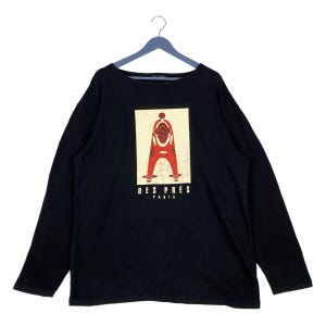 Könnte beinhalten: Schwarzes Langarmshirt mit einem Grafikdruck einer roten Figur mit einem Kreis in der Mitte. Der Text "DES PRÉS PARIS" ist unter der Figur gedruckt.