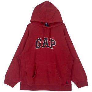 May include: A red hooded sweatshirt featuring the word "GAP" in navy blue and white lettering. It has a front pocket and a drawstring hood. The fabric looks soft and worn. The sweatshirt is a casual style.