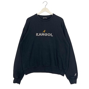 Puede incluir: Sudadera Kangol negra con texto "KANGOL" bordado en blanco y un logotipo de canguro. La sudadera est&aacute; colgada de una percha blanca. Un peque&ntilde;o logotipo de canguro est&aacute; en la manga izquierda.