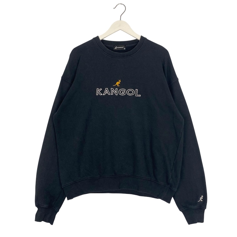 Puede incluir: Sudadera Kangol negra con texto "KANGOL" bordado en blanco y un logotipo de canguro. La sudadera est&aacute; colgada de una percha blanca. Un peque&ntilde;o logotipo de canguro est&aacute; en la manga izquierda.