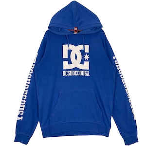 May include: A blue hooded sweatshirt with a white logo on the front and white text on the sleeves. The logo features a stylized "DC" design with a star. The text "DCSHOECOUSA" is below the logo.