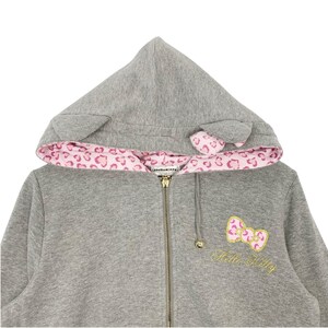 May include: A gray zip-up hoodie with a hood featuring cat ears and a pink leopard print lining. The hoodie has a gold zipper and a Hello Kitty bow applique with gold embroidery. The Hello Kitty logo is embroidered below the bow.