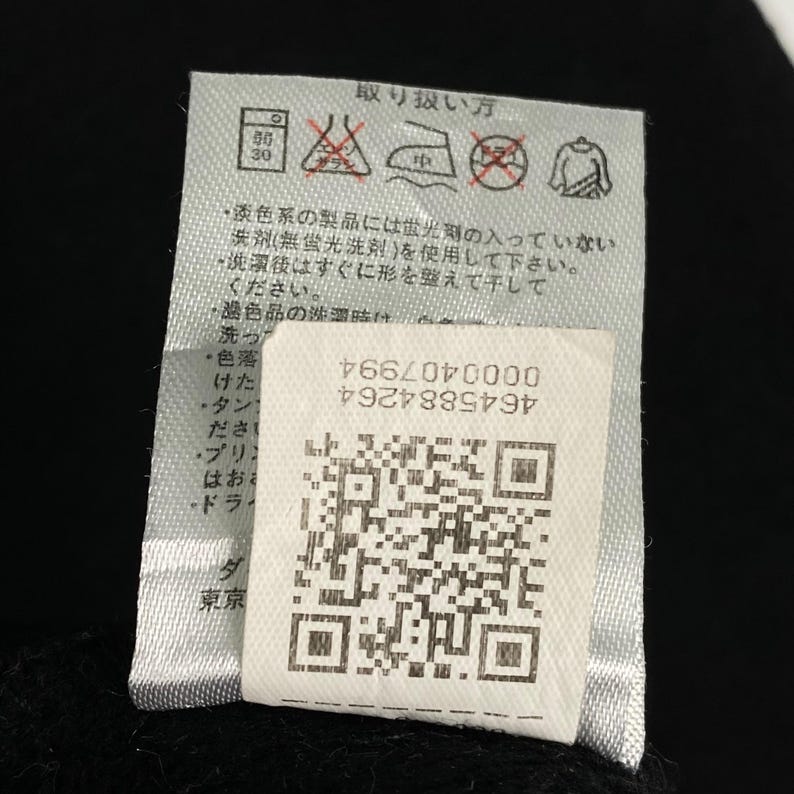 以下が含まれることがあります： 白い洗濯表示タグに黒い文字と記号が書かれています。文字は「取り扱い方」と書いてあり、英語では「Care Instructions」という意味です。タグには洗濯、アイロン、乾燥に関する指示が書かれています。タグにはQRコードも含まれています。QRコードの下の文字は「0000407994 4645884264」です。
