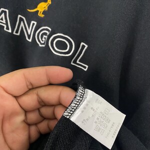 Puede incluir: Sudadera negra con el texto blanco "ANGOL" y un logotipo de canguro amarillo. La sudadera tiene una etiqueta con texto japon&eacute;s e instrucciones de cuidado. La tela parece ser una mezcla de materiales.