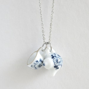 May include: A silver chain necklace with two small porcelain teacups as pendants. The teacups are decorated with a blue and white floral pattern.