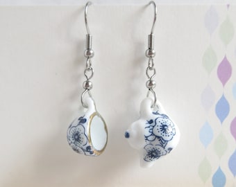 May include: A pair of silver earrings with blue and white porcelain teacups hanging from them. The teacups have a floral design.