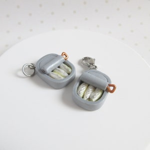 May include: Two silver charm pendants shaped like a can of sardines. Each charm has a small, copper-coloured pull tab and a silver ring for attaching to a chain or bracelet.