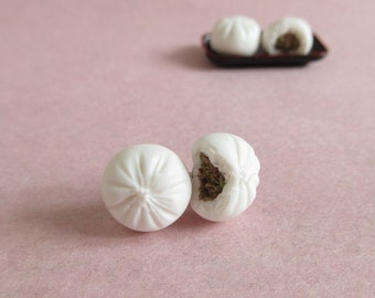Könnte beinhalten: Zwei weiße gedämpfte Brötchen, eines mit einem Bissen herausgenommen, der eine grüne Füllung enthüllt, auf einer rosa Oberfläche.