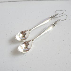 Peut inclure: Une paire de boucles d'oreilles pendantes argentées en forme de cuillères miniatures. Chaque boucle d'oreille présente un long manche fin et un bol arrondi et concave, suspendu à un crochet d'oreille en métal simple et incurvé.