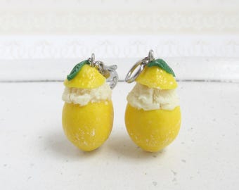 May include: Two yellow lemon charm pendants with green leaves and white frosting. The charms are attached to silver jump rings.