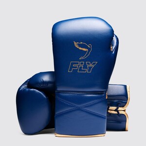 Peut inclure: Une paire de gants de boxe bleu marine avec des bordures dorées. Le mot "FLY" est inscrit en or, accompagné d'un graphisme doré d'oiseau. Les gants sont en matière synthétique lisse. Idéal pour la boxe.