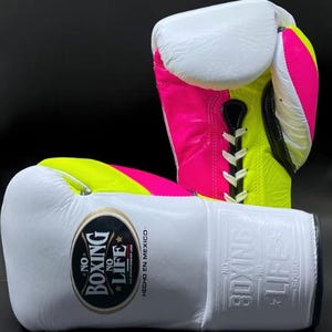 Könnte beinhalten: Ein Paar Boxhandschuhe in Weiß, Neonrosa und Neongelb. Die Handschuhe tragen den Text "NO BOXING NO LIFE" und "HECHO EN MEXICO". Die Handschuhe sind aus Leder und haben einen Schnürverschluss.