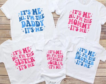 May include: White family matching t-shirts and a onesie with retro text. The shirts read "It's Me, Hi, I'm the Daddy", "It's Me, Hi, I'm the Mommy", "It's Me, Hi, I'm the Sister", "It's Me, Hi, I'm the Birthday Girl", and "It's Me, Hi, I'm the Brother".