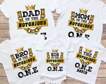 May include: Set of five white t-shirts with gold chain and crown designs. The shirts say "Dad of the Notorious", "Mom of the Notorious", "Bro of the Notorious", "Sis of the Notorious", and "The Notorious".