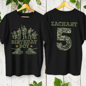 May include: Two black t-shirts with military-themed designs. One shirt features a camouflage design with the text "BIRTHDAY BOY" and images of soldiers and tanks. The other shirt has the name "ZACHARY" and the number "5" in camouflage.