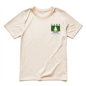 May include: Cream-colored t-shirt with a crew neck. A green square graphic on the chest features a white pine tree, the word "CAMP" above it, and "NAME" below, with blue wavy lines. The shirt is made of a soft material.