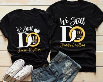 May include: Two black t-shirts with the text "We Still Do" and a gold ring with a diamond. The ring has the number "10" and the word "Years" on it. The text "Jennifer & William" is below the ring on each shirt.