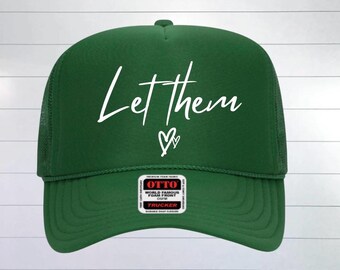 May include: A green trucker hat with the words "Let them" in white script, followed by a heart symbol. The hat has a mesh back and a curved brim. A small patch is visible on the front.