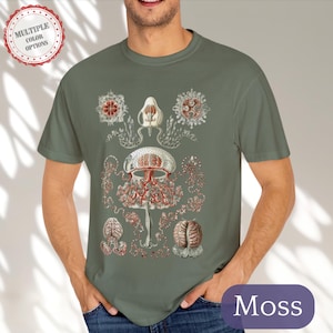 May include: A moss green t-shirt with a vintage illustration of a jellyfish with red and white details. The illustration is centered on the shirt and is surrounded by smaller illustrations of jellyfish.