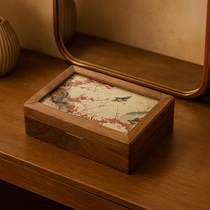 以下が含まれることがあります： 長方形の木製ボックス、ヒンジ付きの蓋付き。 蓋には、鳥と赤い花が描かれた伝統的なアジアの風景の額入りプリントが施されています。 ボックスは暖色系の木材で作られています。