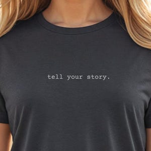 May include: A dark gray t-shirt with the text "tell your story." printed in white on the front.