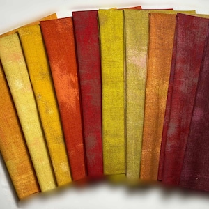 May include: A collection of 10 fabric swatches in various shades of yellow, orange, and red. The fabric has a subtle texture and a faded, distressed look.
