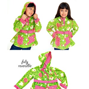 May include: A reversible jacket with a hood, featuring a green and pink floral print on one side and a pink and green geometric print on the other side. The jacket has a belt, buttons, and pockets. The text "fully reversible" is visible on the image.