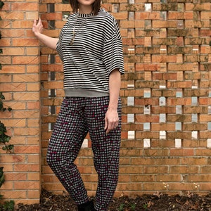 May include: A woman wearing a black and white striped top with a black and white checkered pattern pants. She is standing in front of a brick wall.