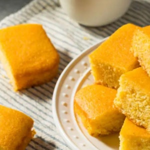 Op de afbeelding: Een bord met vers gebakken maïsbrood vierkanten. Het maïsbrood is goudbruin en heeft een licht kruimelige textuur.