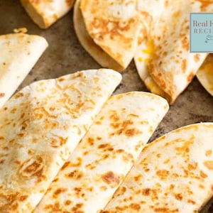 Puede incluir: Vista aérea de varias quesadillas doradas, algunas cortadas en triángulos. Las tortillas tienen un aspecto ligeramente chamuscado con marcas de parrilla visibles. La imagen incluye un pequeño cuadrado con el texto "Real Food RECIPES".