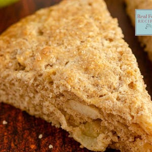 Könnte beinhalten: Eine Nahaufnahme eines goldbraunen Scones mit flockiger Textur. Der Scone ist dreieckig geschnitten und hat eine sichtbare Apfelschicht im Inneren. Der Scone liegt auf einer braunen Holzoberfläche.