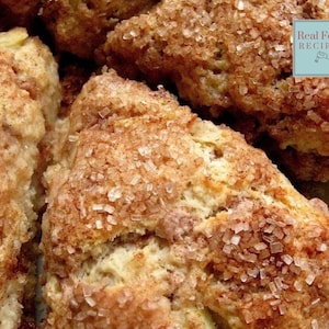 Könnte beinhalten: Nahaufnahme von mehreren gebackenen Scones, jeweils mit goldbrauner Außenseite und einer großzügigen Beschichtung aus groben Zuckerkristallen. Die Scones sind dreieckig und scheinen frisch gebacken zu sein, mit einer leicht bröseligen Textur. Das Bild enthält den Text "Real Food Recipes".