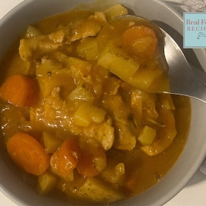 Puede incluir: Un cuenco de estofado con trozos visibles de zanahorias, patatas y carne en una salsa espesa de color marrón dorado. Una cuchara está sacando una porción del estofado. La imagen incluye un logotipo de Real Food Recipes.