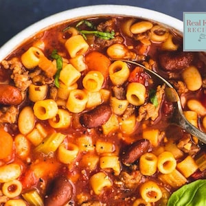Peut inclure: Un gros plan sur un bol de soupe italienne de mariage copieuse avec des pâtes, des haricots, des légumes et de la viande. La soupe est rouge et savoureuse, et les pâtes sont en forme d'anneaux. Une cuillère est partiellement immergée dans la soupe.