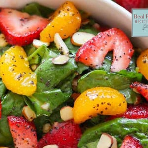 May include: A close-up of a salad with spinach, mandarin oranges, strawberries, and almonds. The salad is topped with poppy seeds. The text "Real Food Recipes" is in the upper right corner of the image.