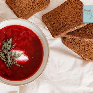 Könnte beinhalten: Eine Schüssel rote Rote-Bete-Suppe mit einem Klecks Sauerrahm und frischem Dill darauf. Die Suppe wird mit Scheiben dunklem Roggenbrots serviert. Rezepte für echtes Essen.