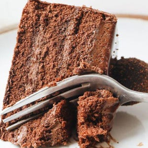 Könnte beinhalten: Eine Nahaufnahme einer Gabel, die einen Bissen von einem Schokoladenkuchen nimmt. Der Kuchen ist mit Schokoladenfrosting geschichtet und hat eine satte, dunkelbraune Farbe.