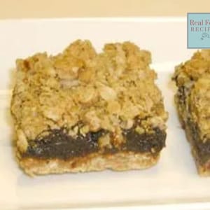 May include: Close-up of three square baked goods on a white plate. The desserts have a dark brown filling, a light brown base, and a crumbly, golden-brown topping. The image includes a small, light blue square with the text "Real Food RECIPES".