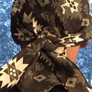 May include: A black and white patterned bandana tied around a person's head. The bandana has a geometric design with white stars and diamonds on a black background.