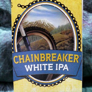 May include: A yellow notepad with a black spiral binding. The front cover features a blue and yellow illustration of a bicycle wheel with the text "Chainbreaker White IPA".